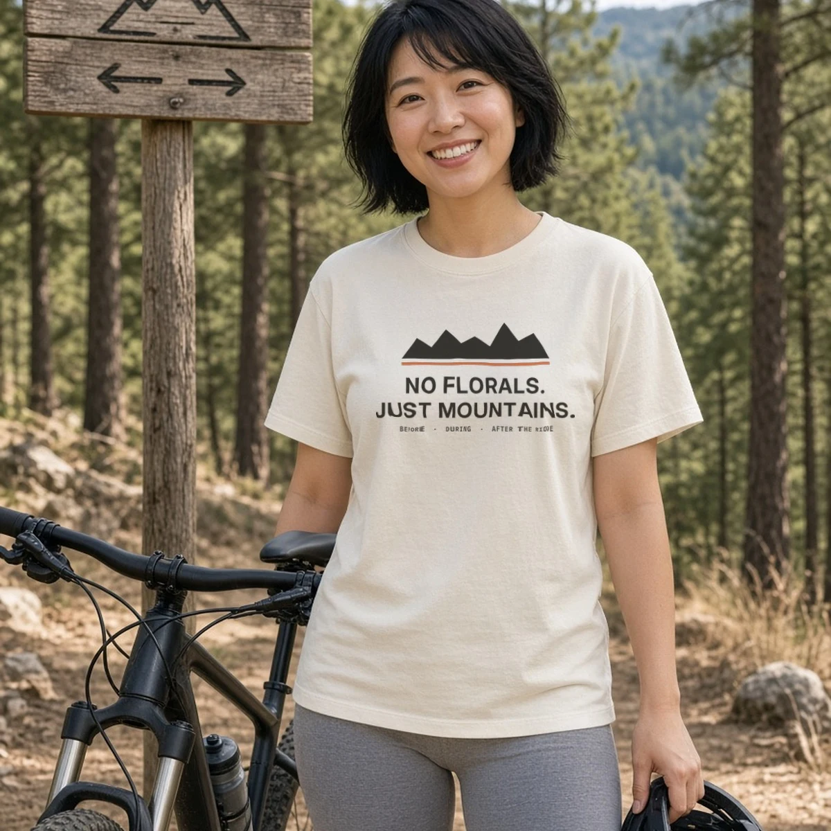 Model wearing the No Florals. Just Mountains. tee in Natural at a trailhead